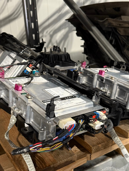 Modules de batterie de véhicule avec câblage et connecteurs, placés sur une palette en bois dans un atelier.